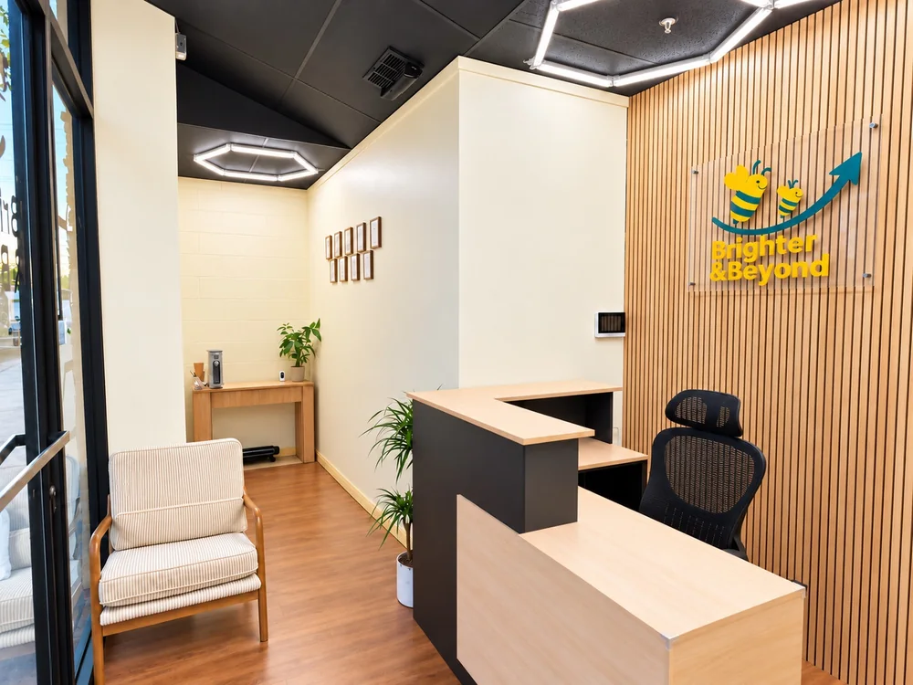 Reception desk, family seating, and Brighter & Beyond bee logo on a wood-paneled wall